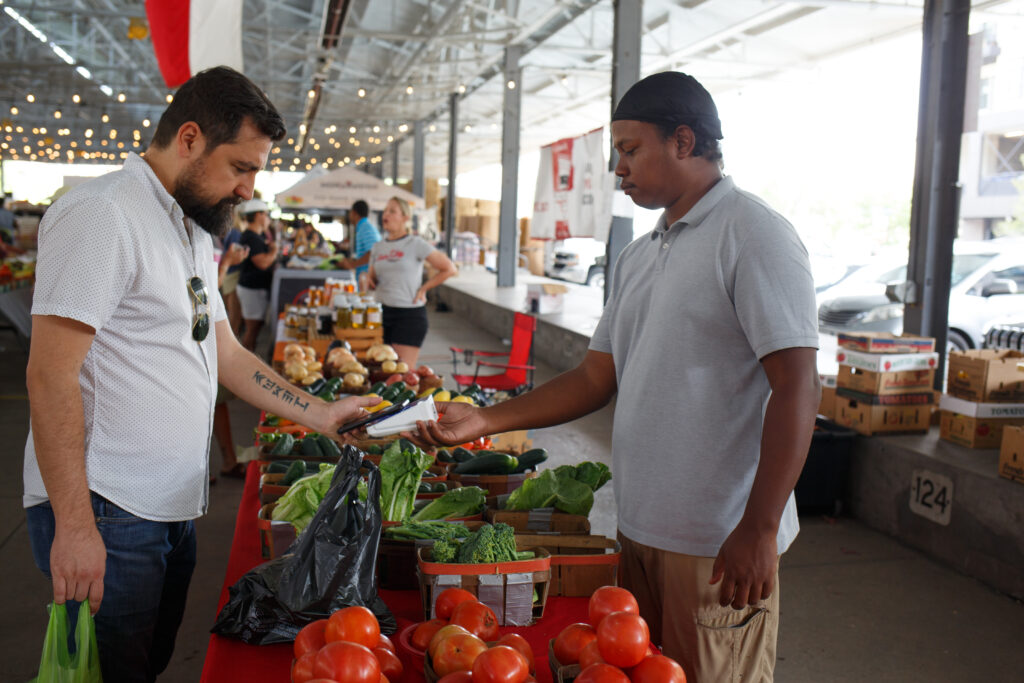 At a farmers market, a customer uses a phone to pay for fresh produce