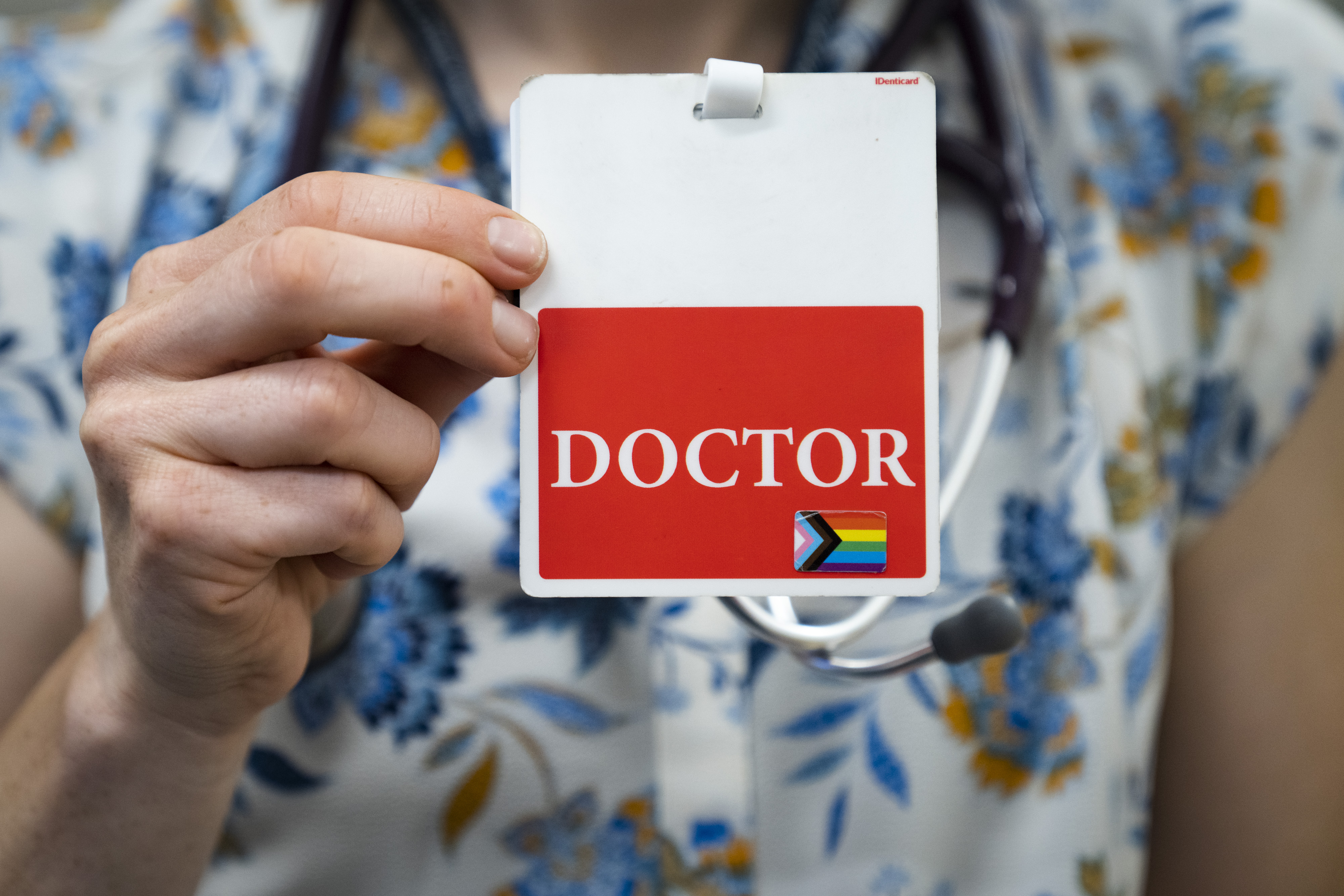 Anna Casell, a newborn medicine doctor, holds up the backside of her name tag which reads "doctor" and has a pride flag sticker