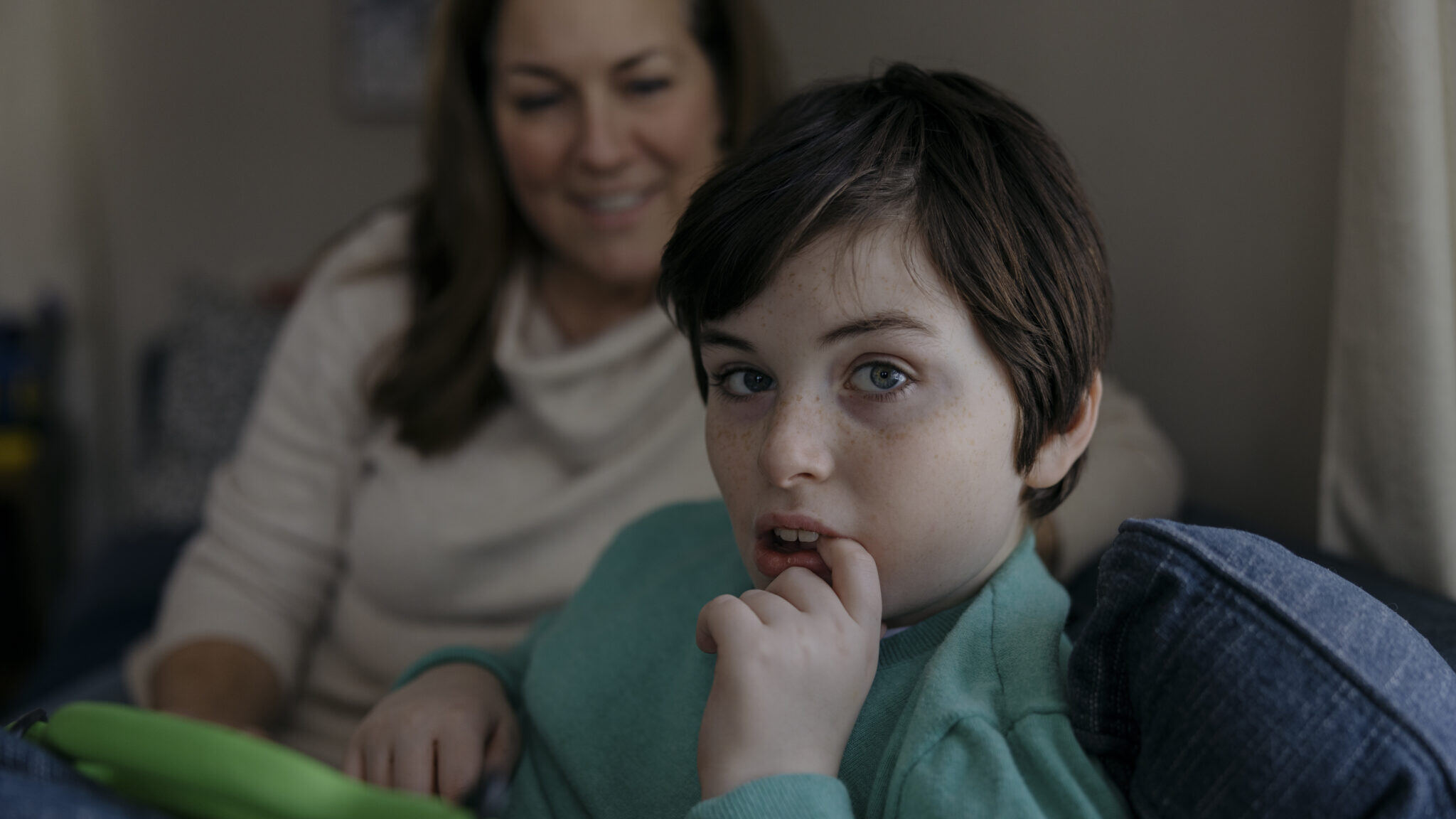 Cristina sits in the background, out of focus, while her 12-year-old son, who suffers from epilepsy, looks directly at the camera. 