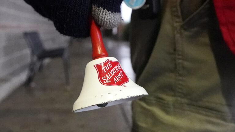 A gloved hand holds a bell with the Salvation Army's logo. Typically seen outside grocery stores around the winter holidays as the group solicits donations.