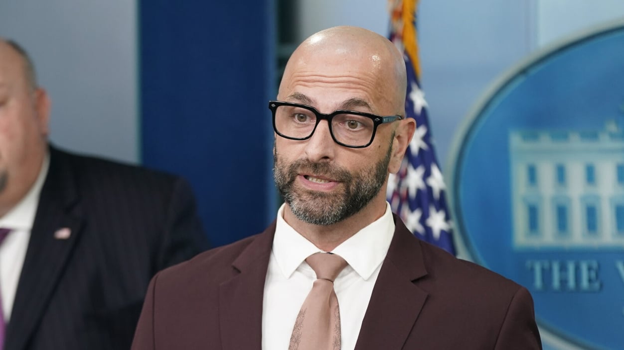 Demetre Daskalakis speaks at the White House in 2022. He wears black thick rim glasses and a maroon suit.