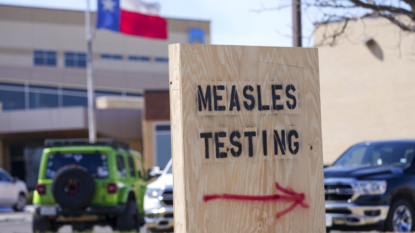 A spray painted, wooden sign that says "measles testing" with a spray painted arrow pointing to the right.