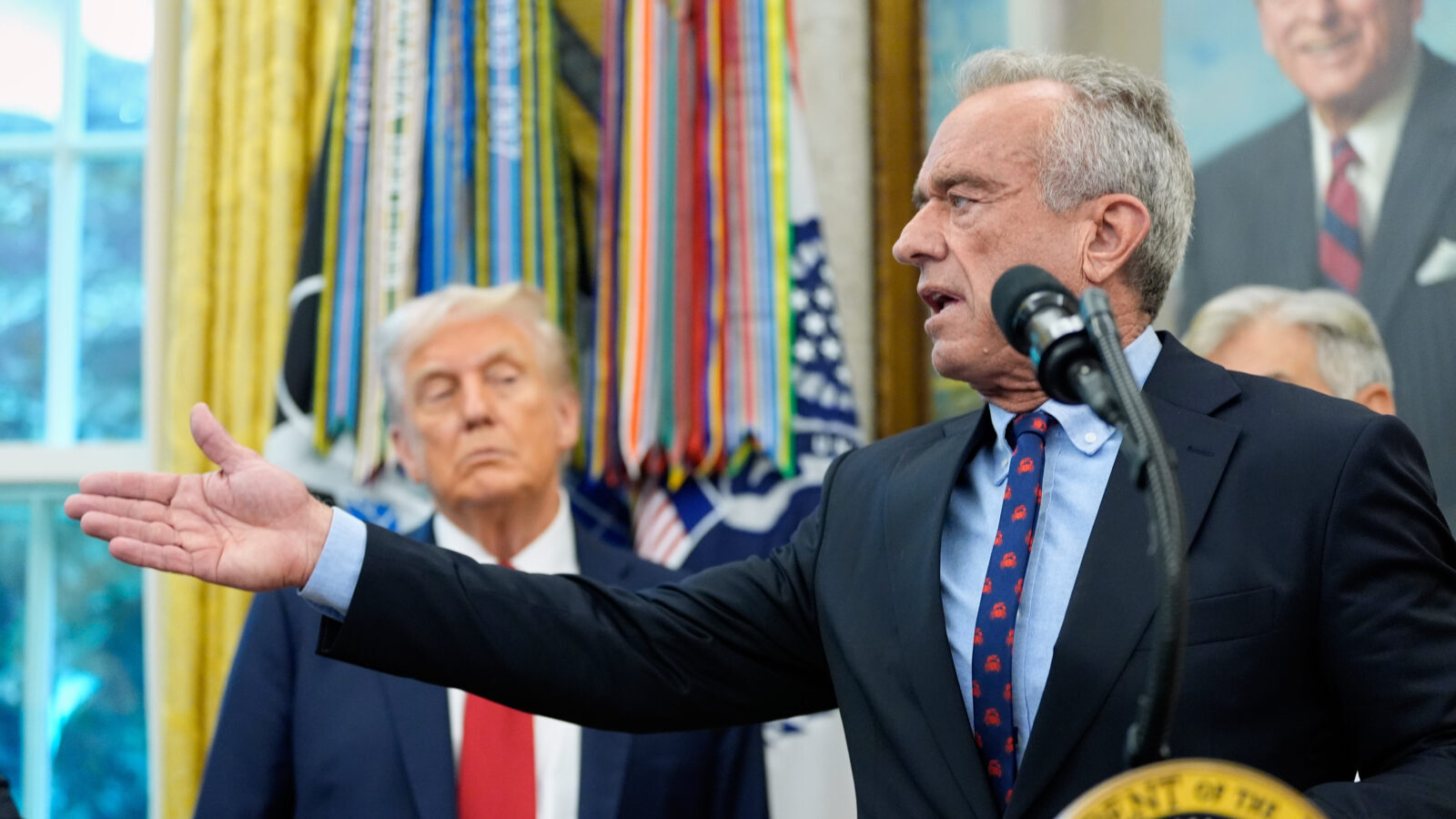 RFK Jr. points, Trump stands behind him lookin skeptical.