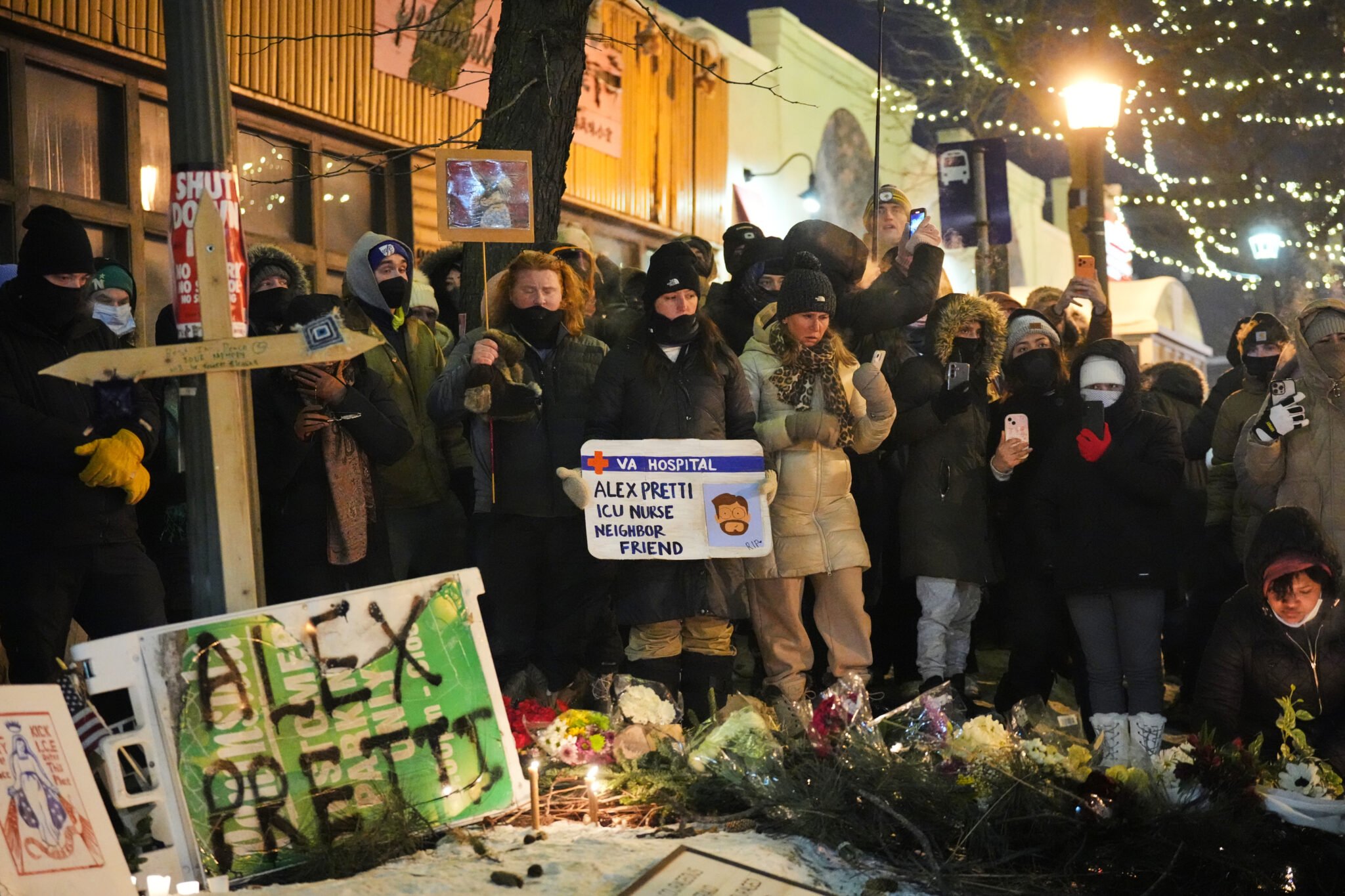 Mourners gather around the site of Alex Pretti's killing. There's a cross, a bunch of flower bouqets, and signs, including one identifying Pretty as an ICU nurse, neighbor, and friend.