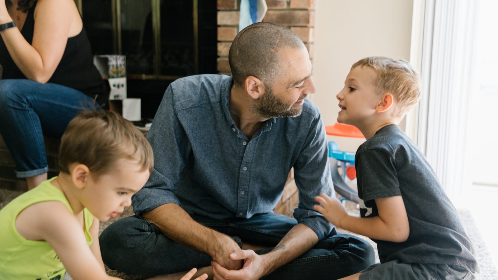 Adam Hayden sits on the floor playing with two of his children.