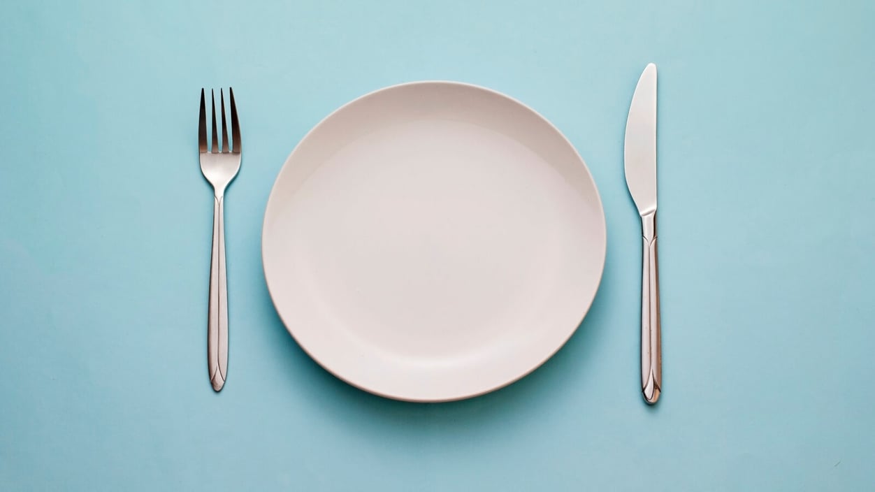 An empty plate with a fork and spoon oagainst a blue background