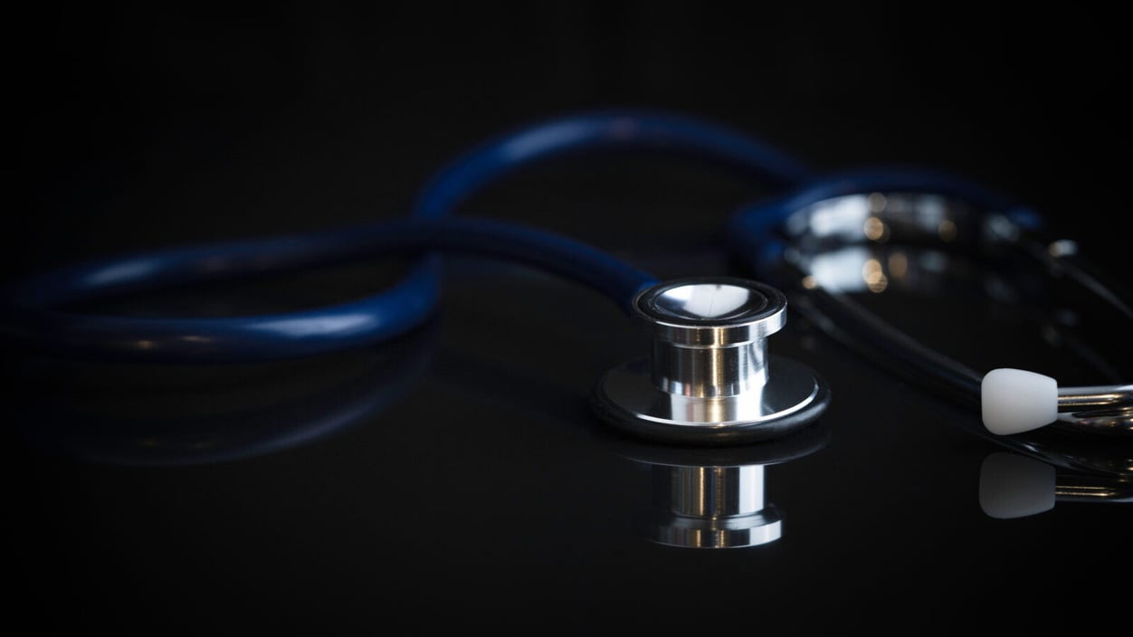 a "moody" stethoscope lays facedown on a black surface, in shadow