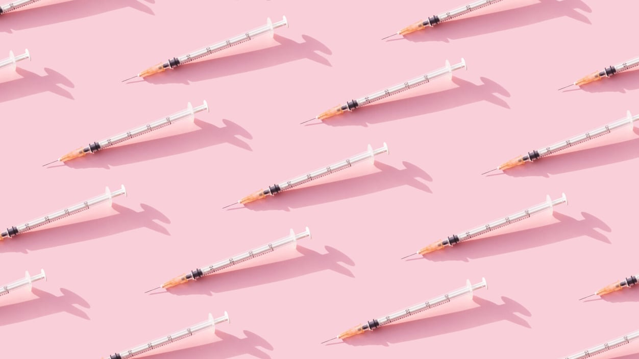 A stock image of needles lined up in rows against a pink background