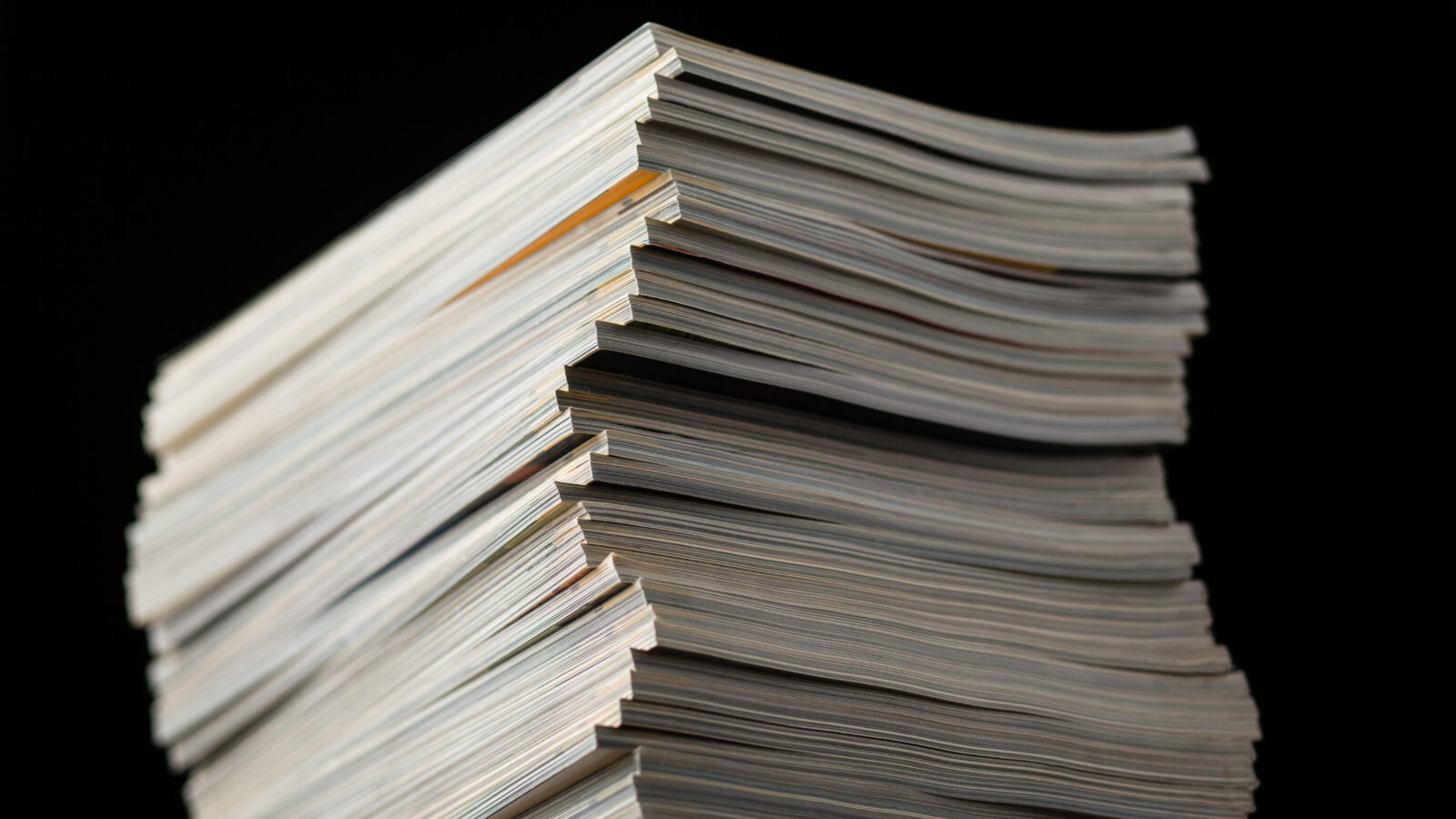 Stock photograph of a tall pile of journals or magazines on a black background