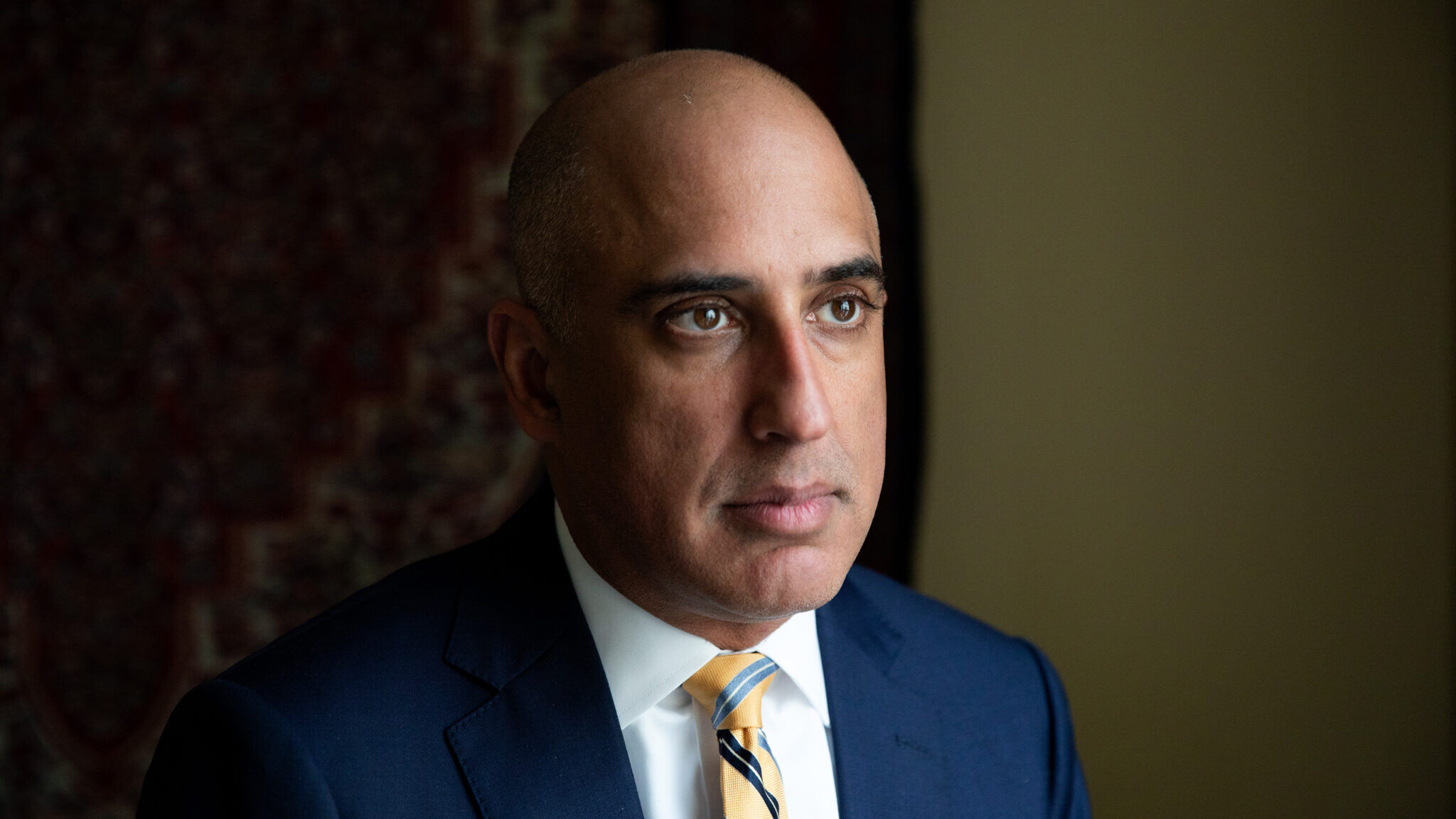 A portrait Ateev Mehrotra wearing a blue suit, white shirt, and yellow striped tie.