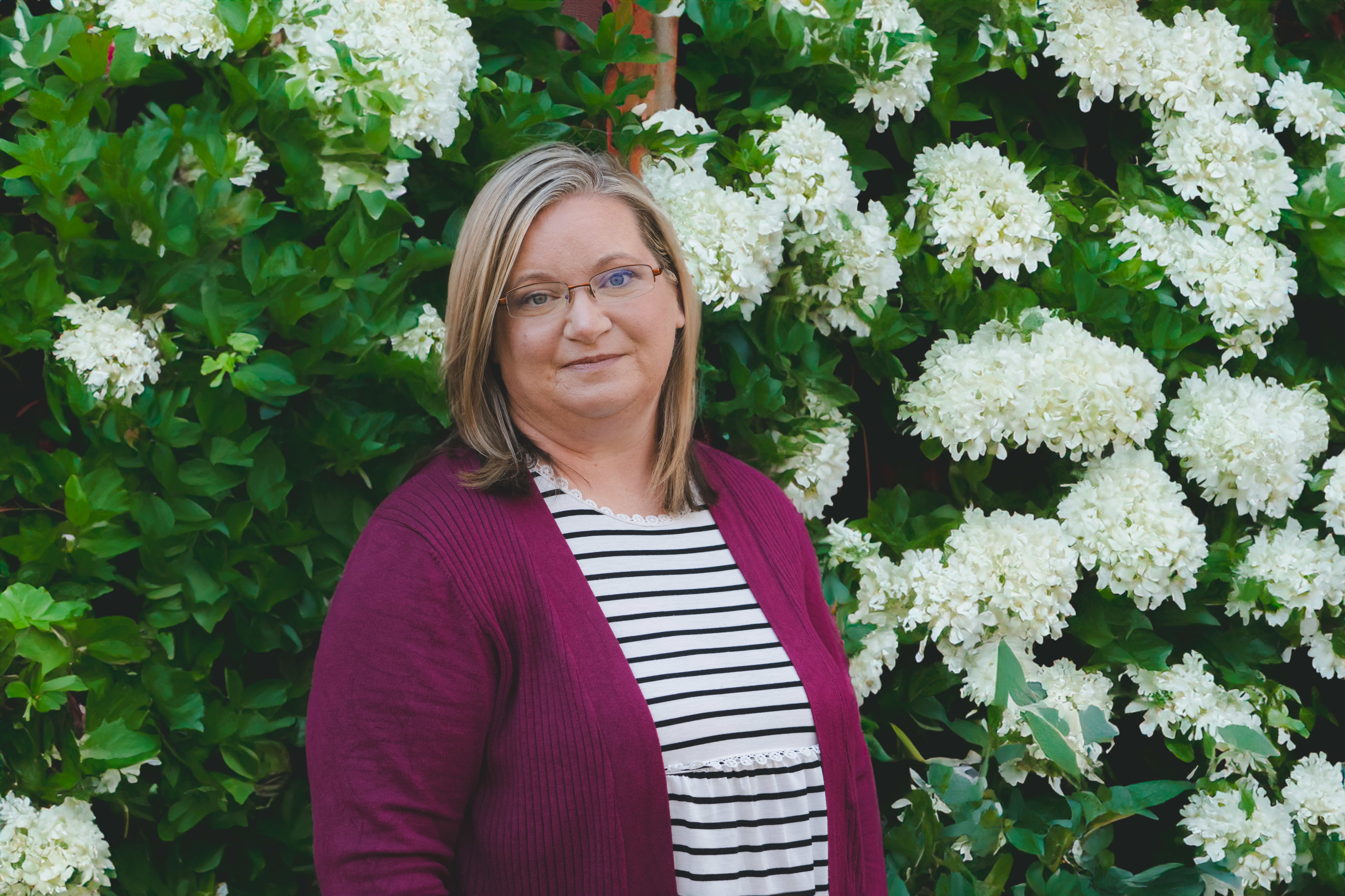 Kristina Dulaney stands in front of bush with white flowers at her home in Telford, Tennessee. 