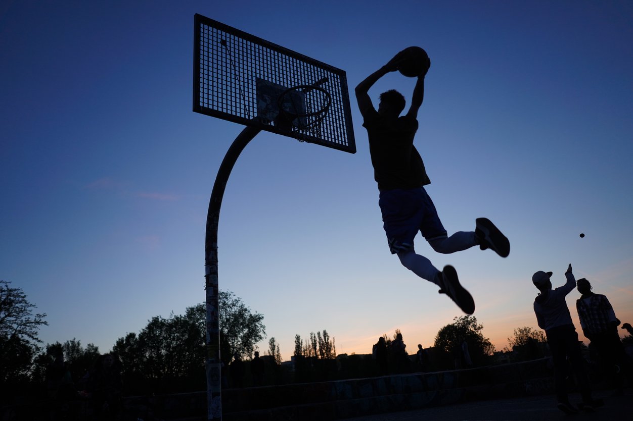 Silhouettes of a person dunking and two people in the background, all against the evening sky in saturated blue and light orange