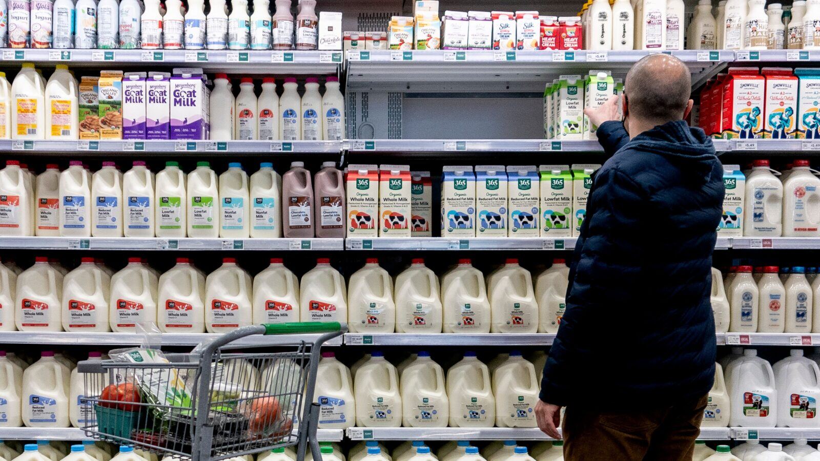 A man picks out a carton of milk from a row of shelves.