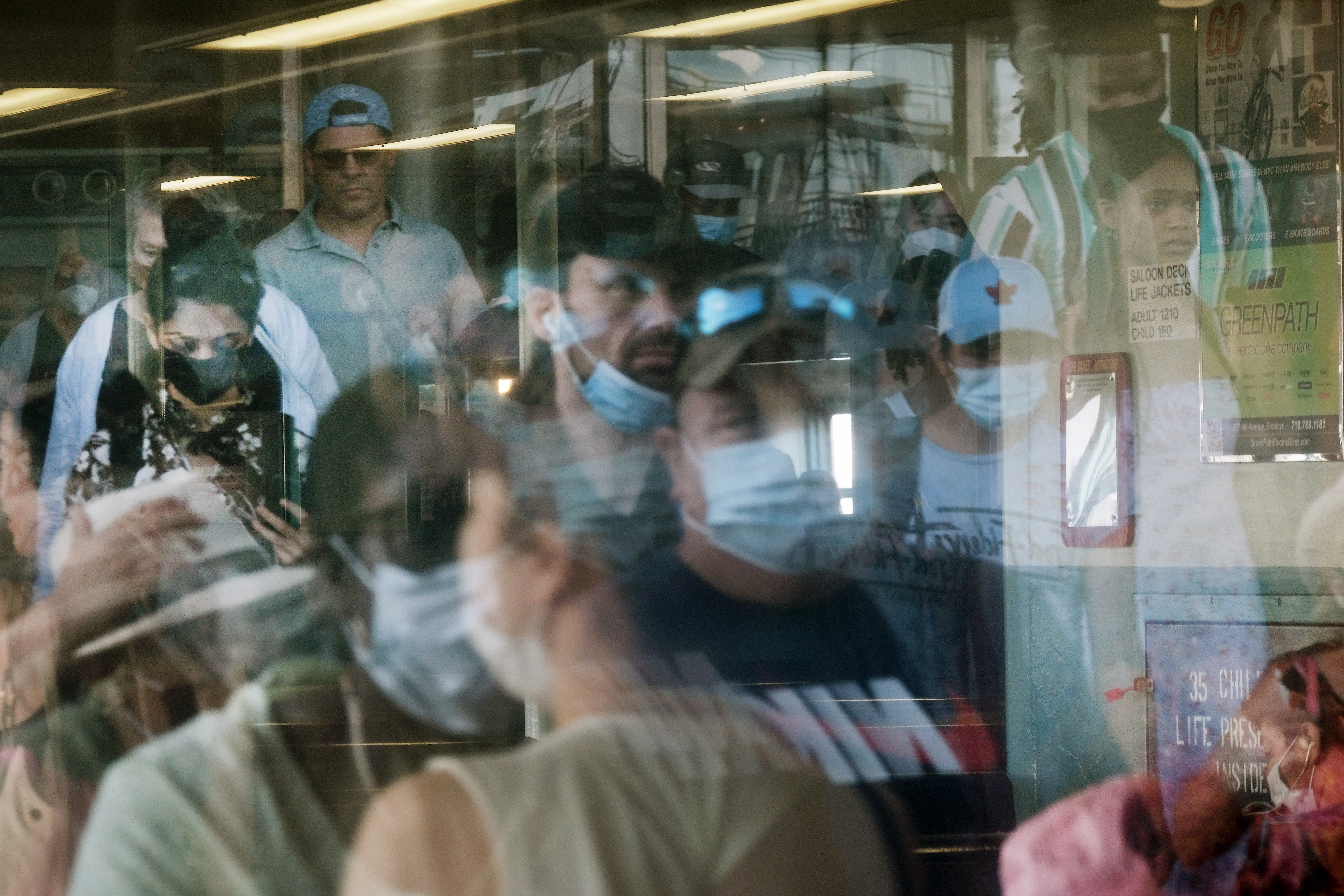 A crowd of people reflected in a windowing some wearing masks, some without.