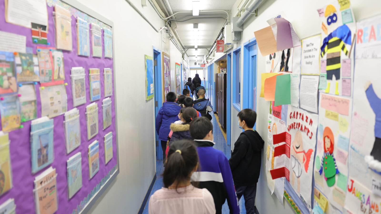 Children walk down a long hallway with walls covered in colorful paper. 