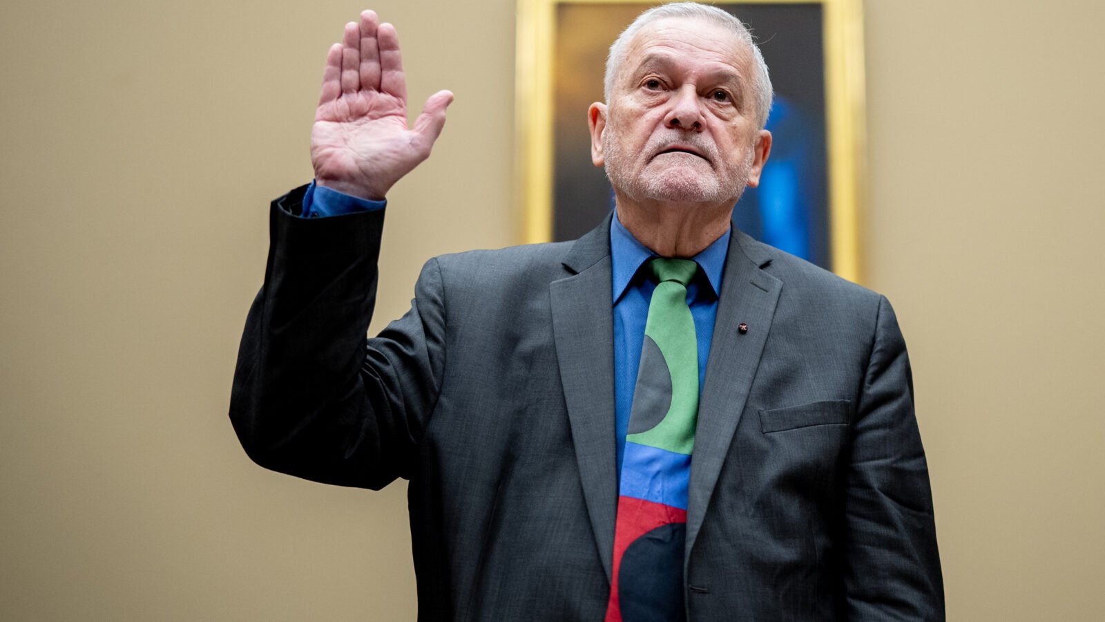 David Morens stands with one hand raised, under oath