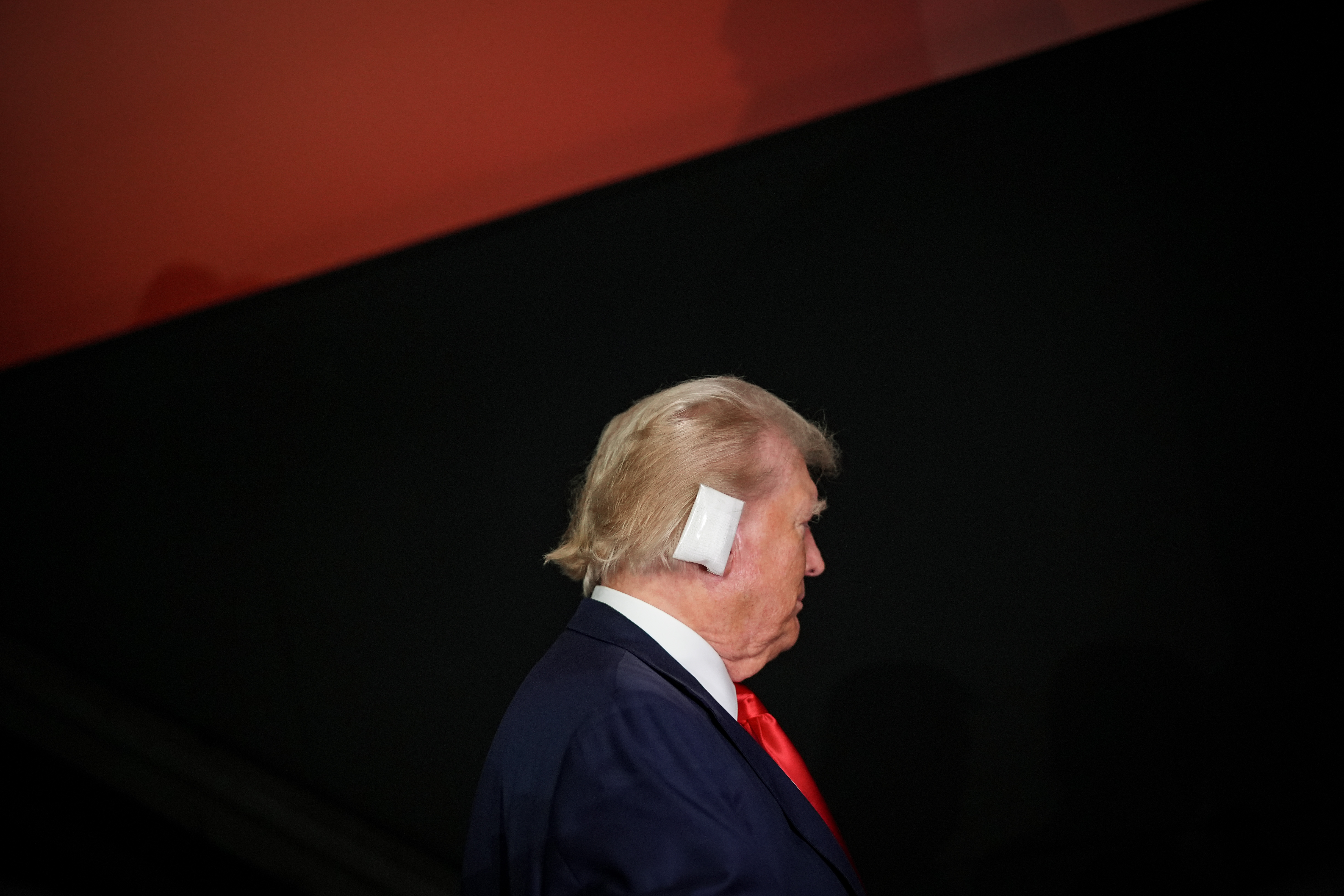 Profile of Donald Trump with a bandaged ear against a red and black background.