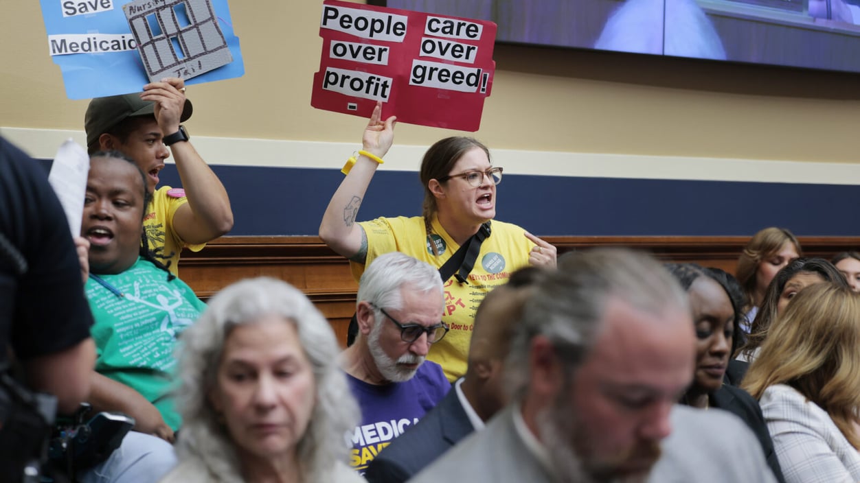 A group of disabled activists protest with signs during a House committee meeting in May.