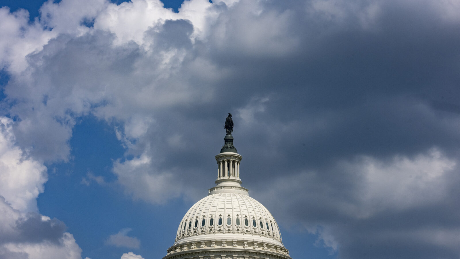 The dome of the Capitol building in DC, with the female figure "Statue of Freedom" on top are center frame against a blue but cloudy, stormy sky.