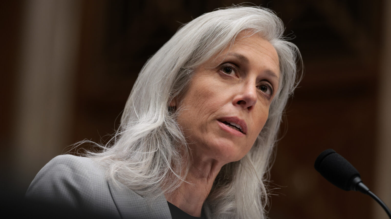 Susan Monarez has long grey hair and speaks at a microphone. The camera is at a steep diagonal angle.
