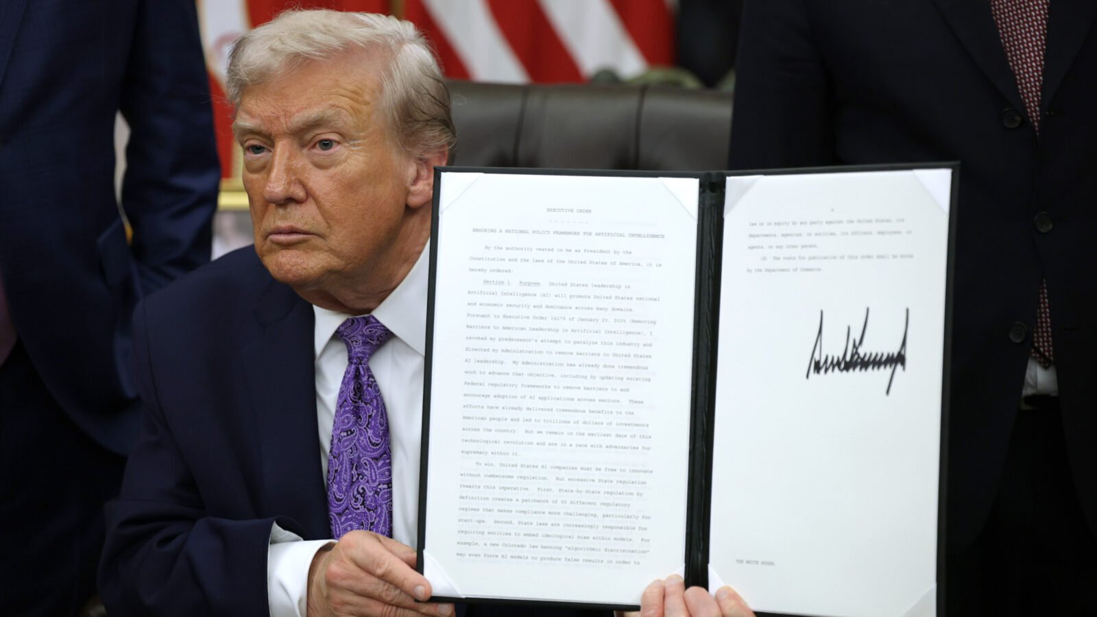 President Trump sits holding up the text of an executive order. He does not smile.
