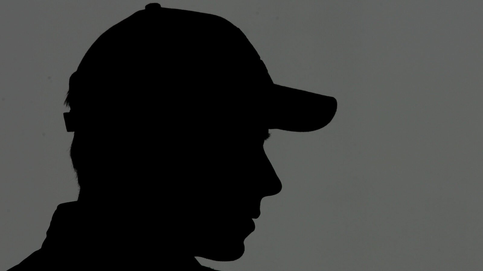 The shadowed outline of a person, likely male, wearing a baseball hat