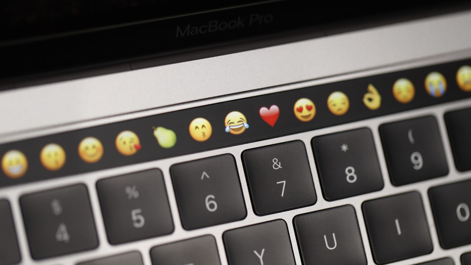 A close up of a keyboard with a row of emojis in the touch screen tool bar at the top.