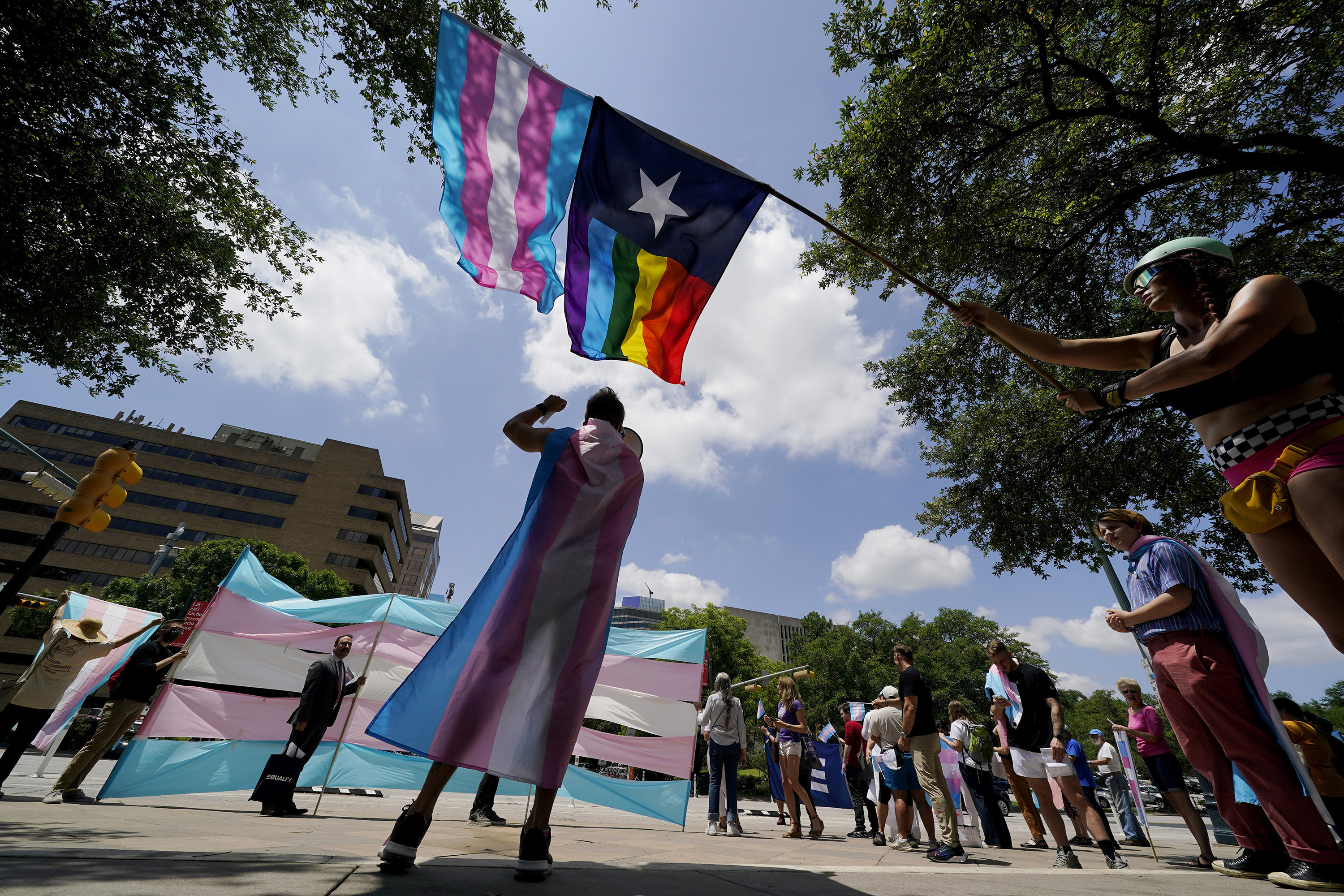 Demonstrators wear and raise transgender flags, along with a pride texas flag