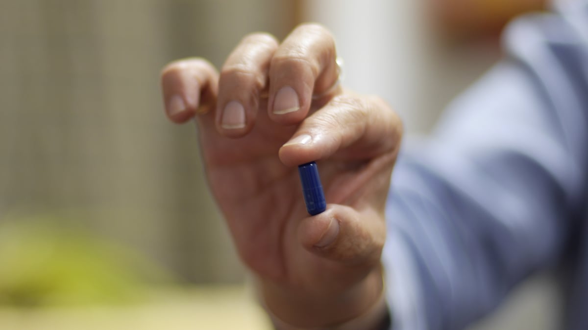 Patient holds blue pill in hand.