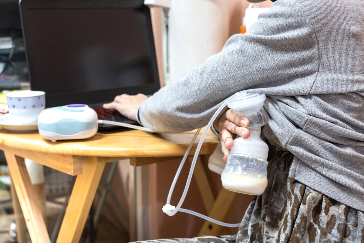 Photo of a mother pumping breastmilk at a table while working on her laptop. 