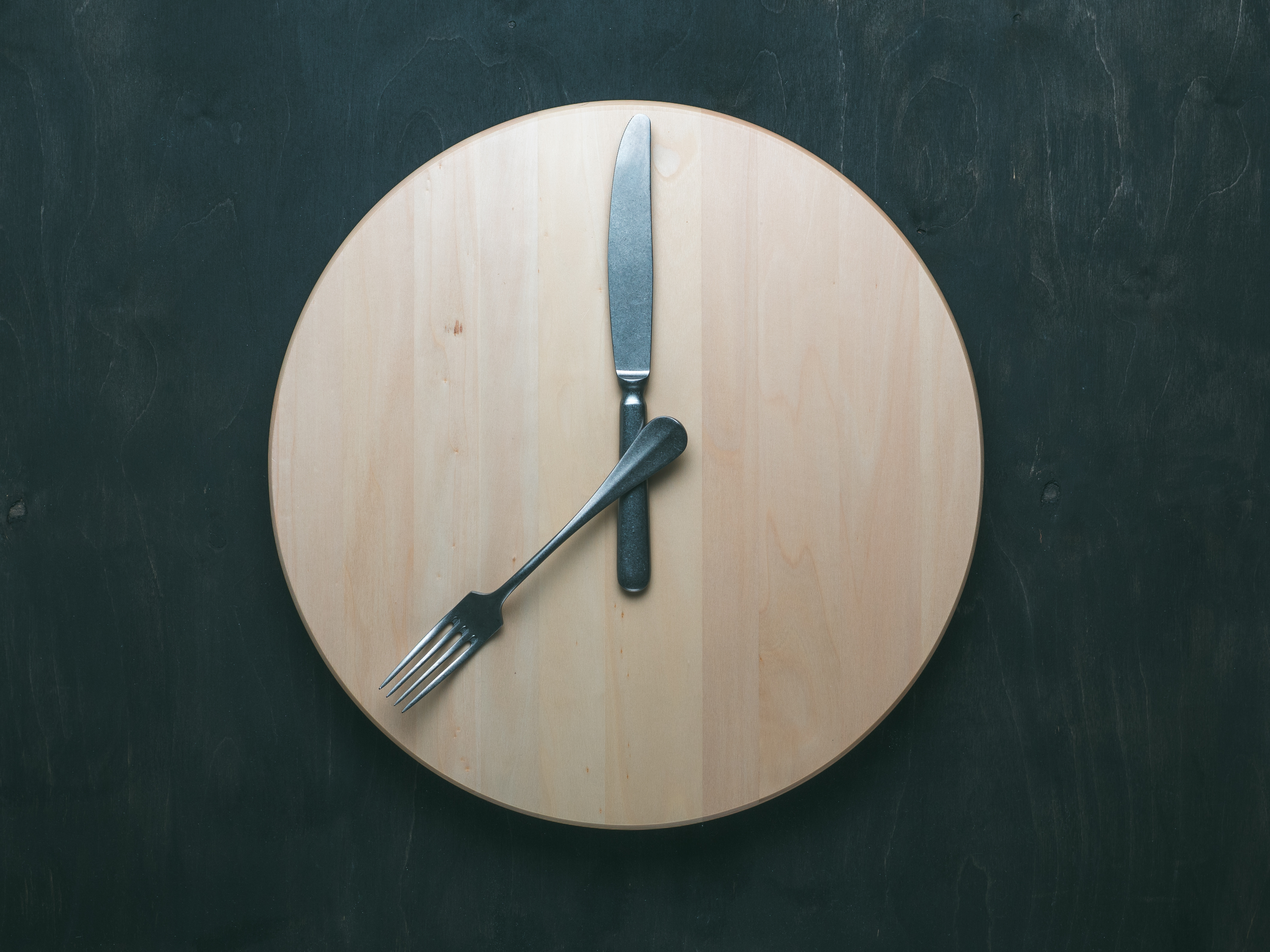 empty wooden round tray with a fork and butter knife as clock hands.