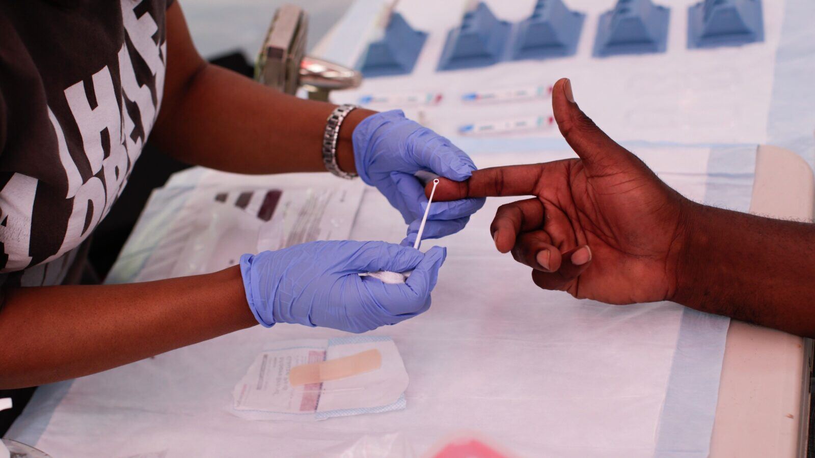 A medical staff holds a person's index finger, extracting blood for an HIV test