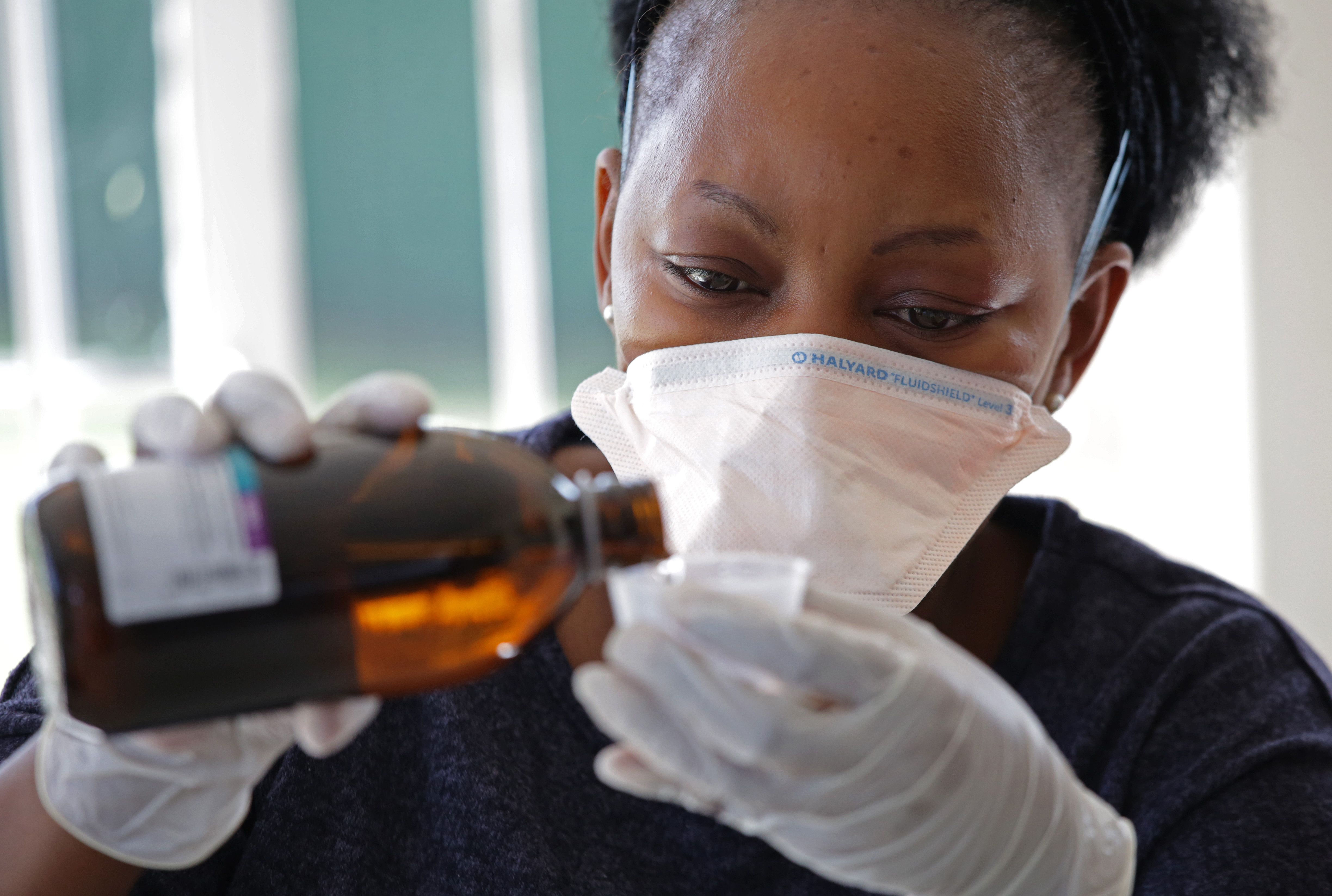 a health professional holds a plastic cup with one hand and pours Methadone Oral Solution in the cup