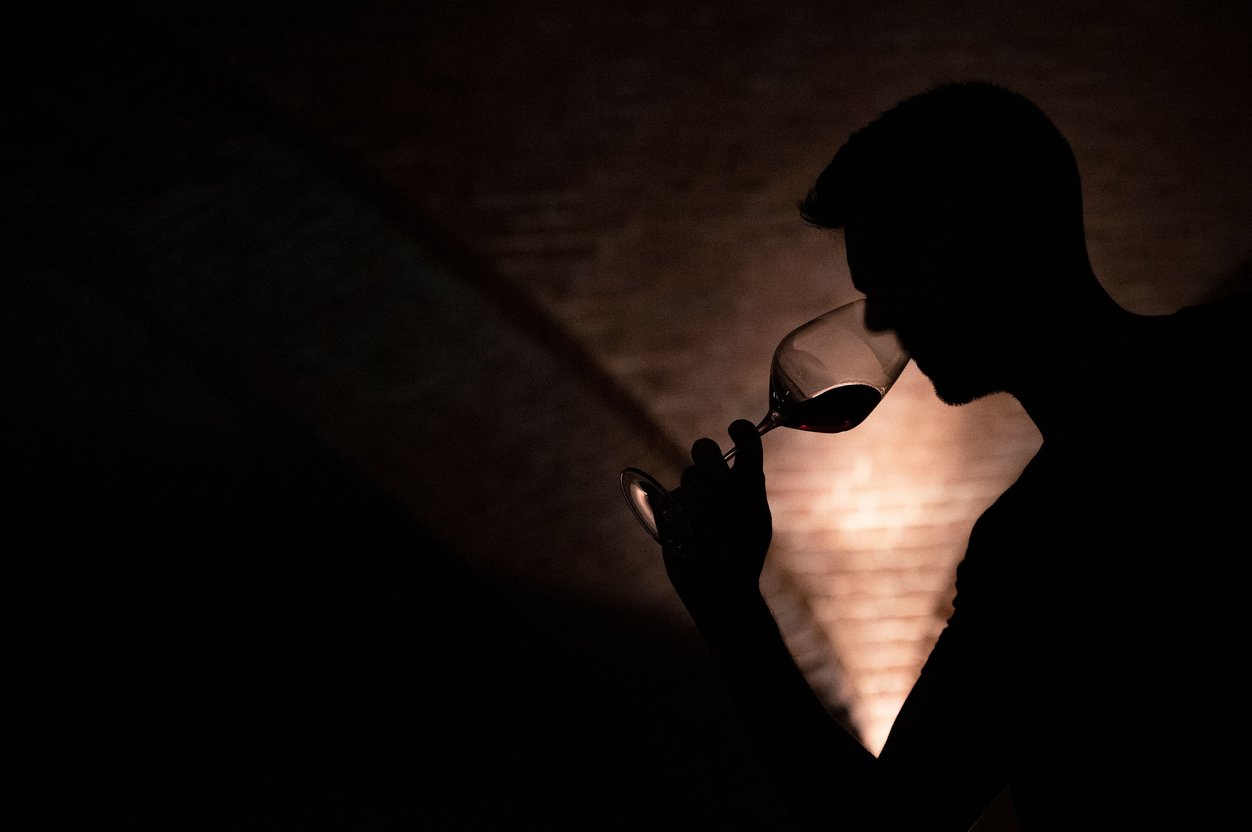 Silhouette of a person with short hair taking a sip of red wine in a winery