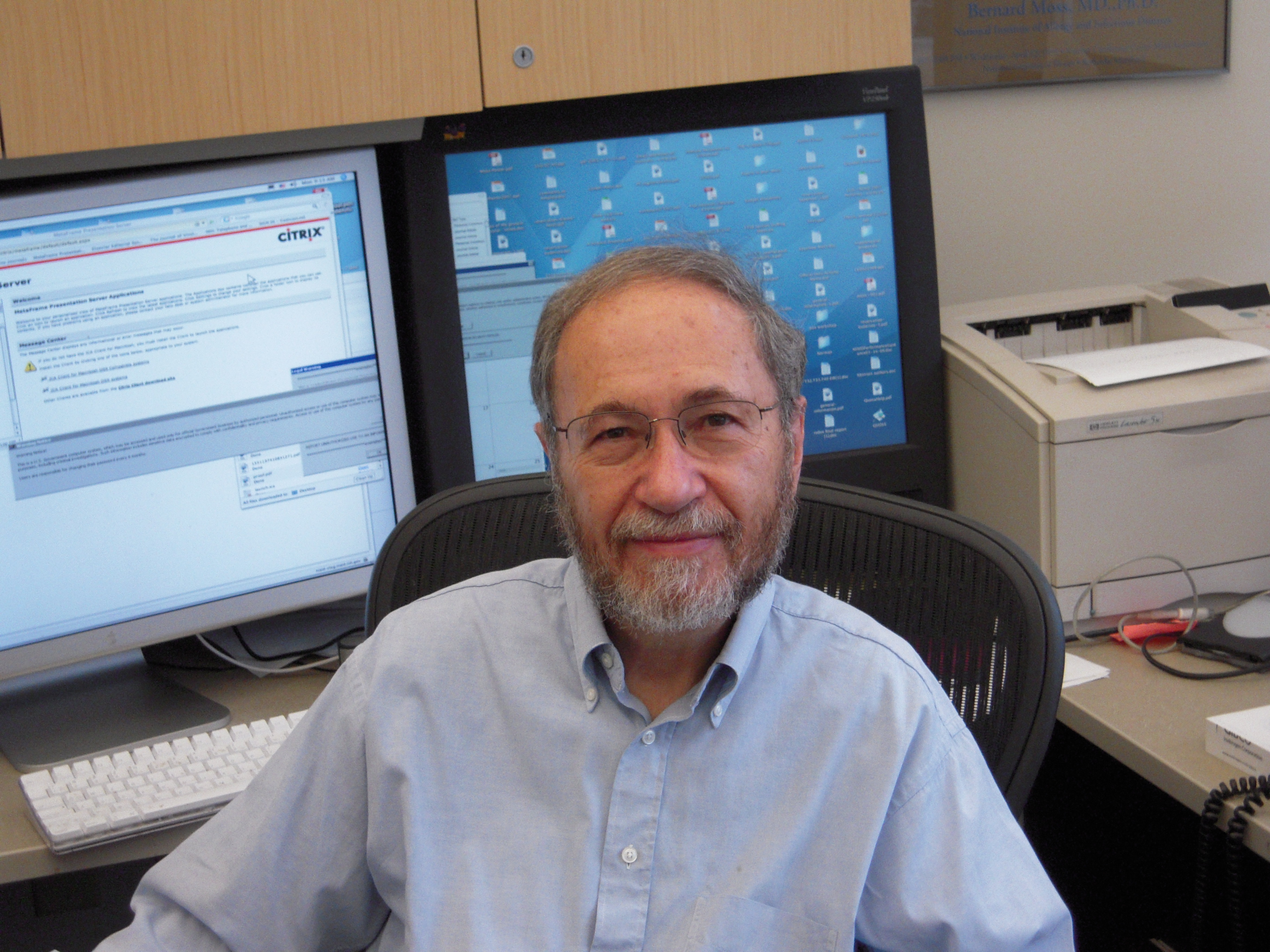 Photo of Bernard Moss sitting in desk chair in front of two computer monitors