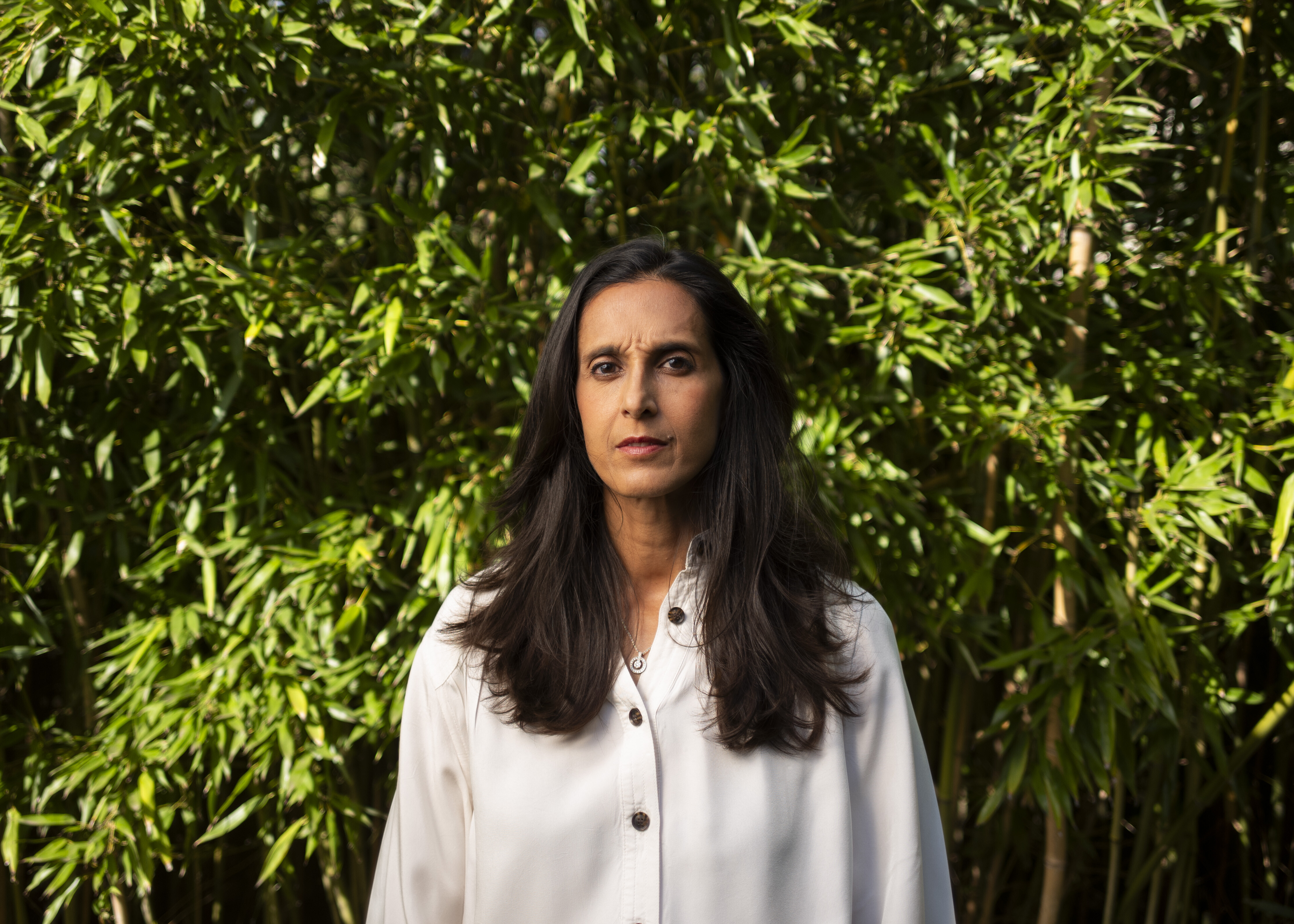 Portrait of Sonya Borrero, who is wearing a white button-down shirt and standing in front of trees.