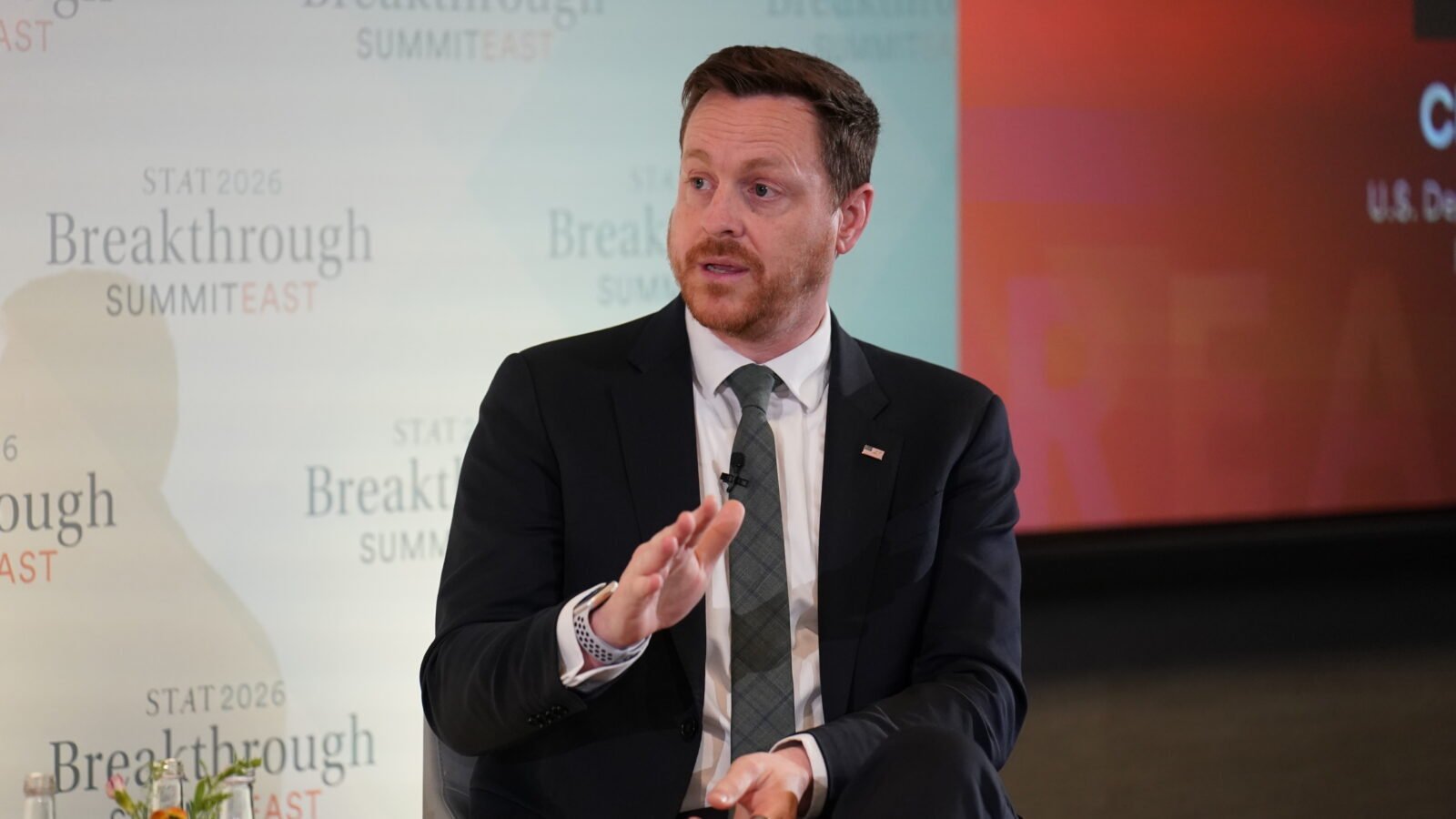 Chris Klomp speaks at the Summit. He's wearing a suit, tie, and an American flag pin. 