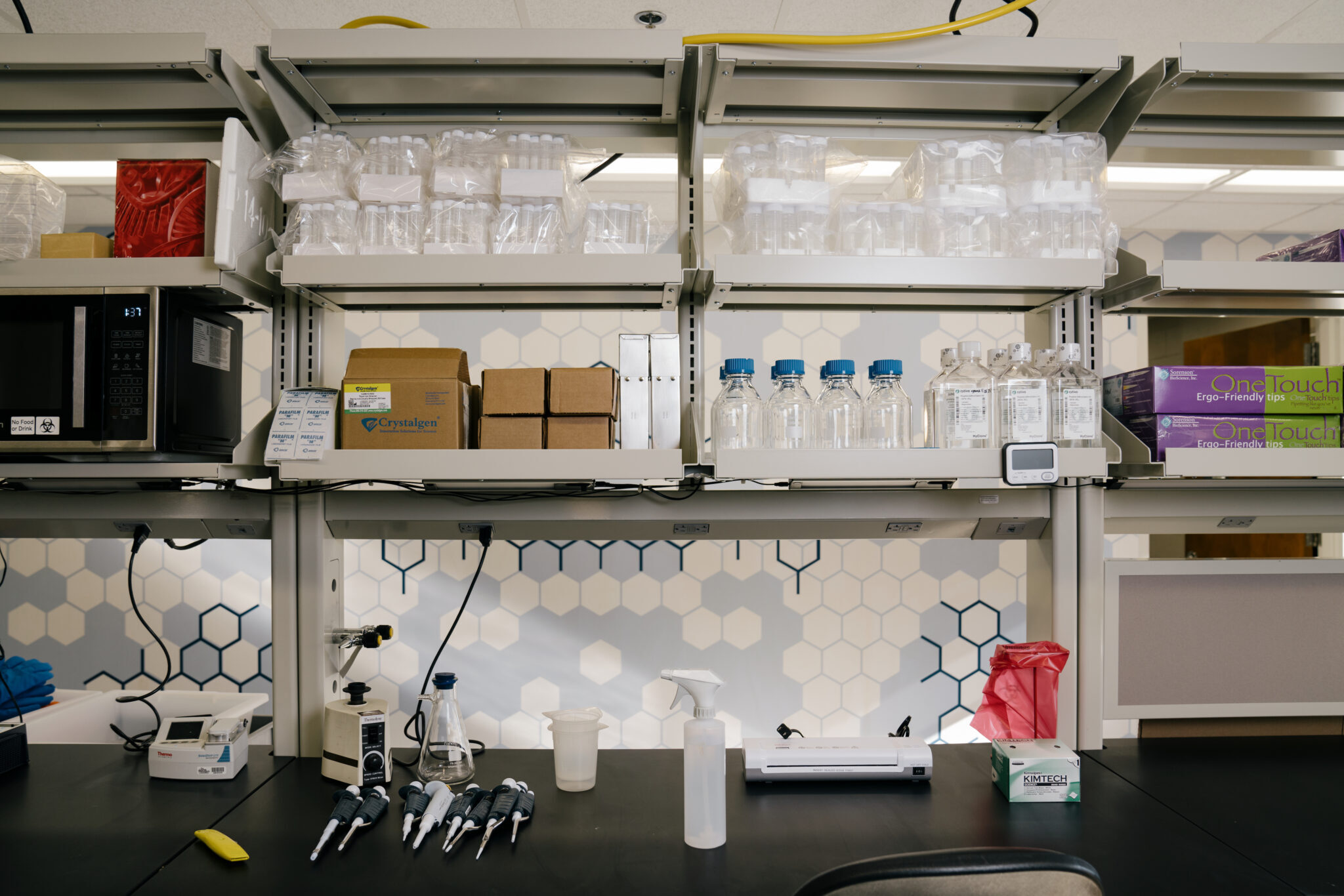 A clean, black counter with clean materials and shelves full of empty bottles and beakers