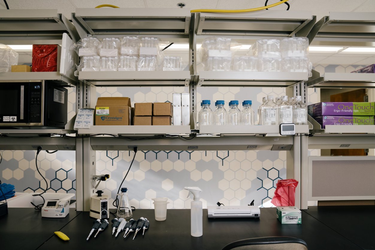 A clean, black counter with clean materials and shelves full of empty bottles and beakers