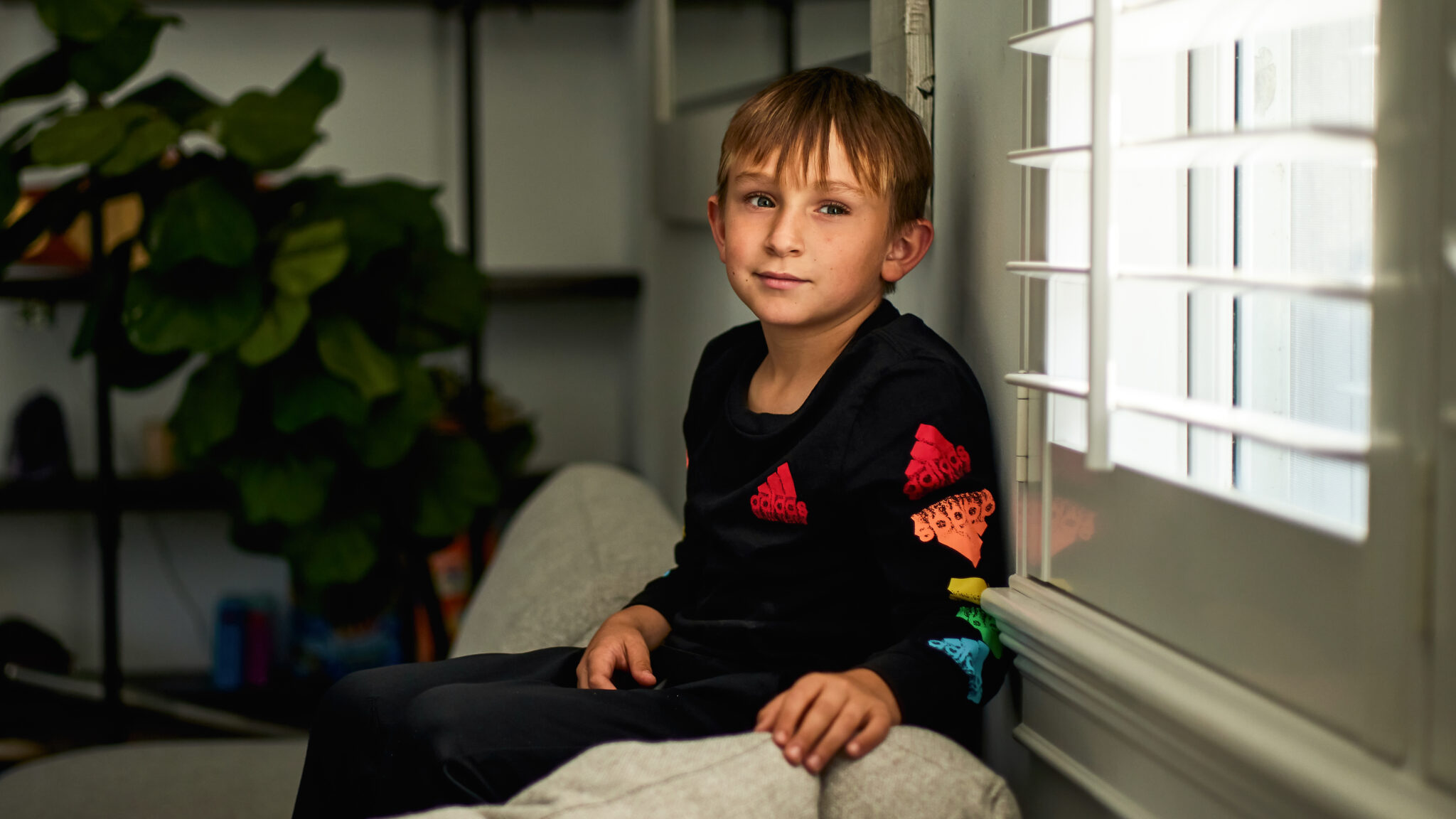 Logan Jenner poses for a portrait sitting on a couch, near a window.