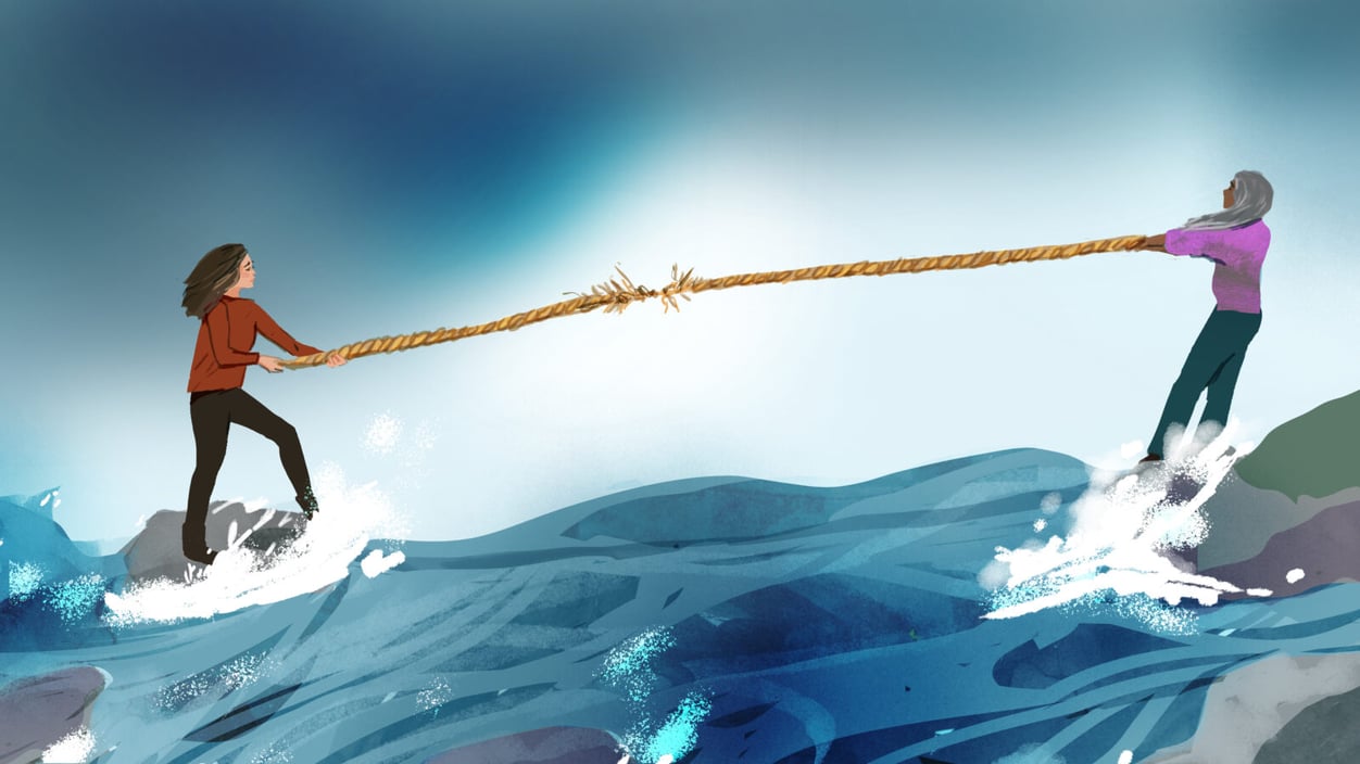 Two people with long hair hold either end of a thinning, about-to-snap rope, tug of war style. They each stand on rocks in a wild sea.