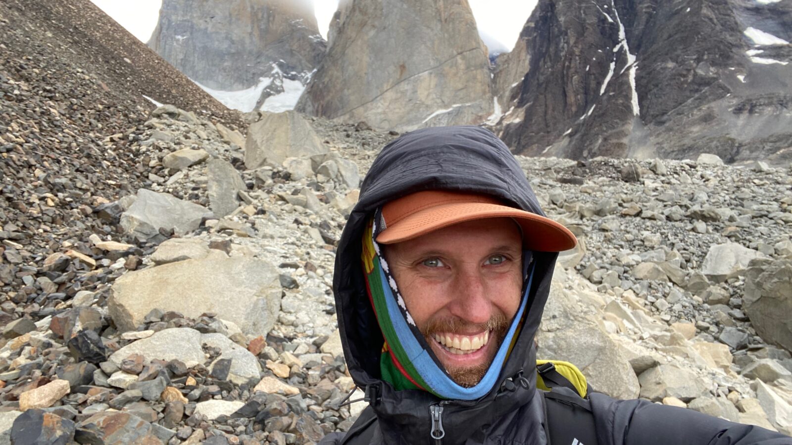 Jeff Vierstra takes a selfie on a mountain, with his hood up, a baseball hat on, and a scarf wrapped around his ears.
