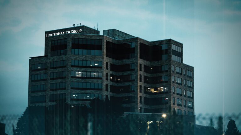 The UnitedHealth Group office building stands tall and dark against a pale blue sky.