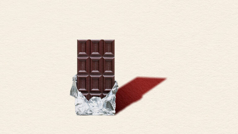 A chocolate bar stands tall, peeled half out of its shell, its shadow falling behind it.